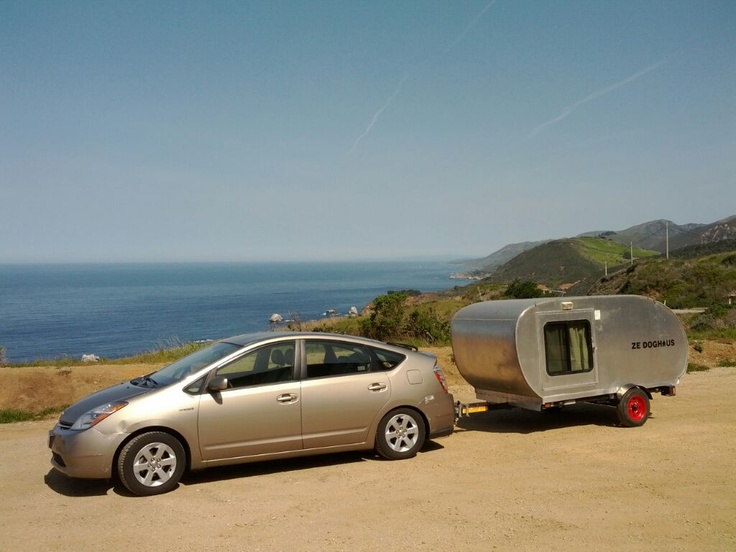 a small silver car parked next to a trailer on the side of a road near the ocean