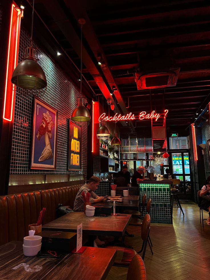 people sitting at tables in a restaurant with neon lights hanging from the ceiling and paintings on the walls