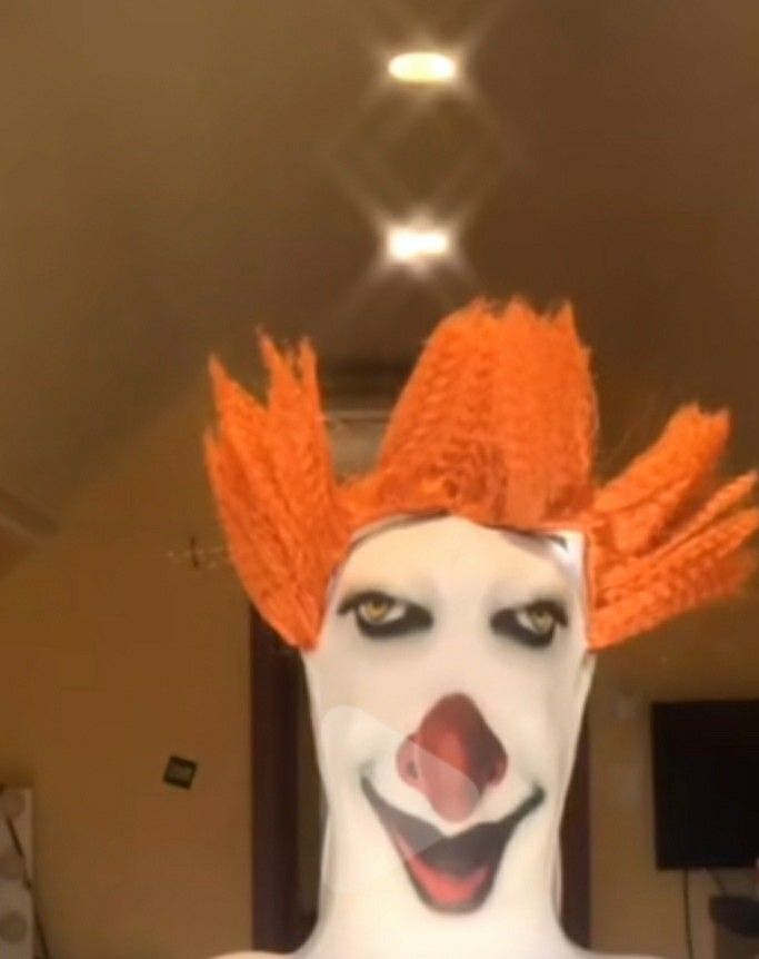 a white clown with orange hair and makeup