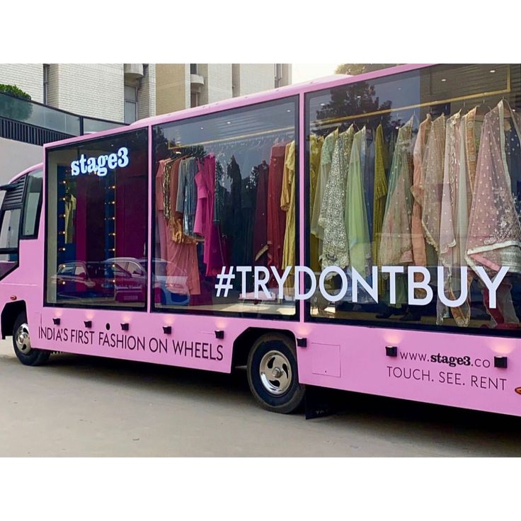 a pink bus that is parked in front of a building with clothes on display and the words tryontbuy written on it