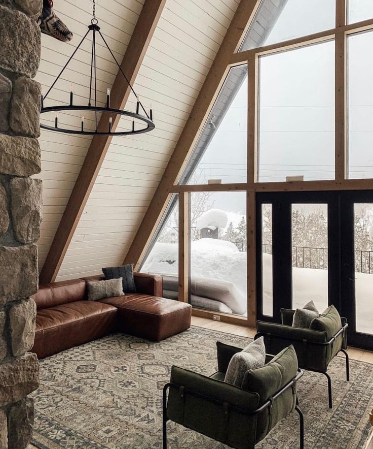 a living room filled with furniture next to large windows and a stone wall covered in snow