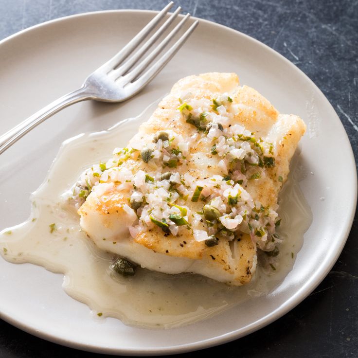 a white plate topped with fish covered in gravy and sauce next to a fork