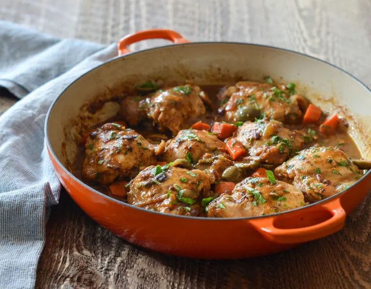 an orange pan filled with meat and veggies on top of a wooden table