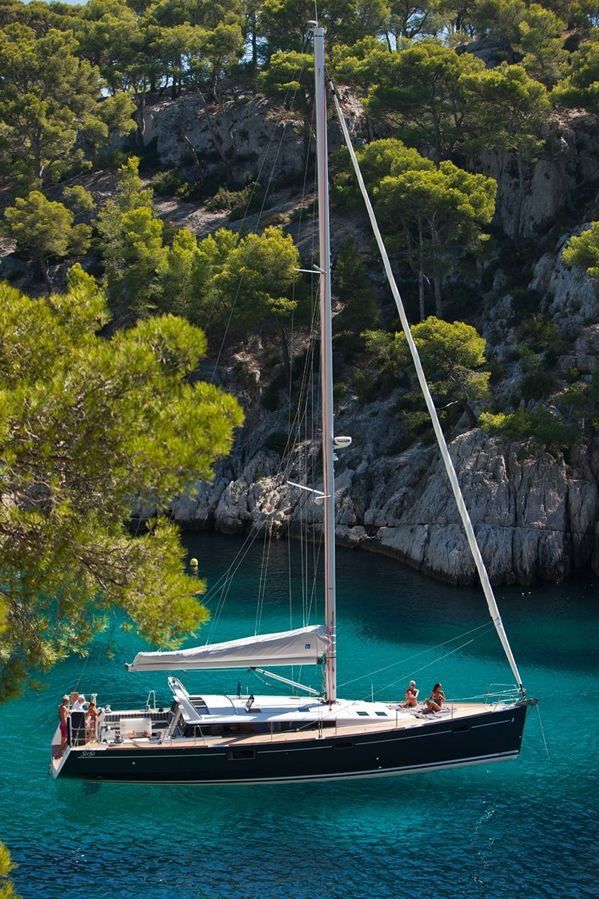 a sailboat in the water with people on it near some rocks and trees,