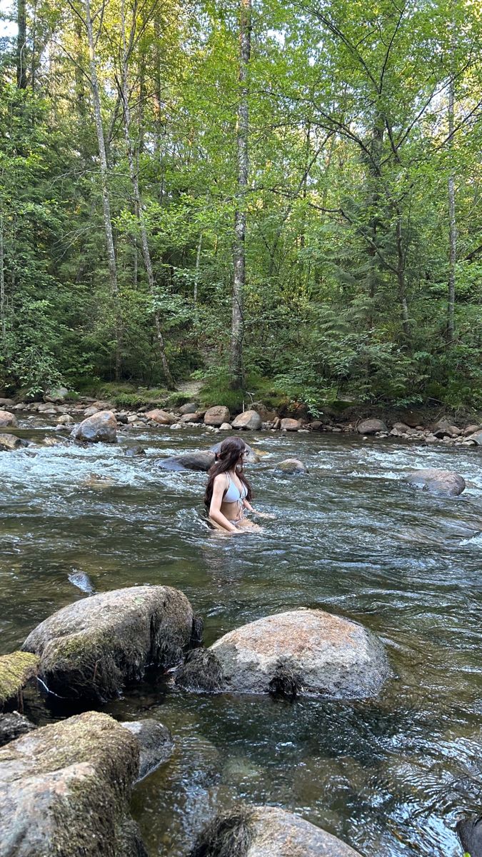 a woman wading through a river surrounded by rocks