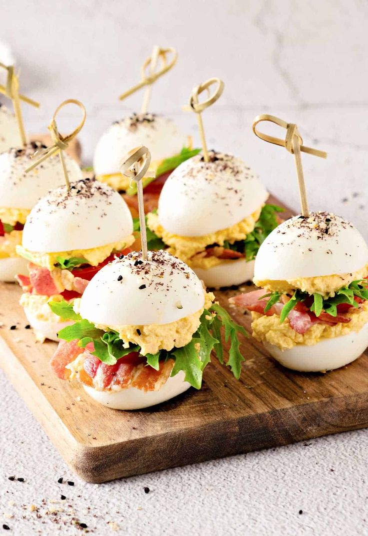 small sandwiches are arranged on a cutting board with toothpicks sticking out of them