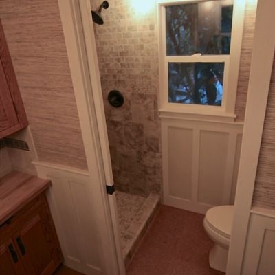 a bathroom with a toilet, sink and shower in it's stall area next to a window