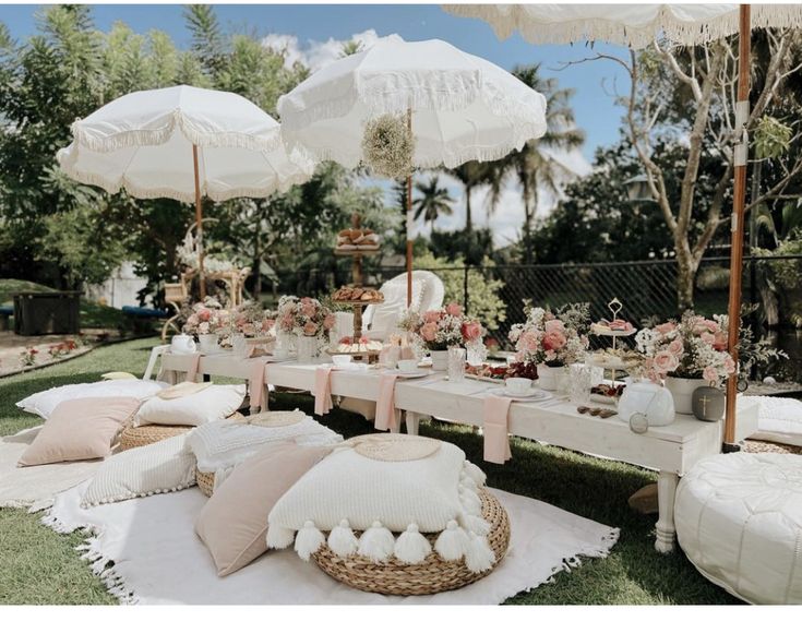 an outdoor picnic setting with white umbrellas and pink flowers on the table, all set up for a tea party