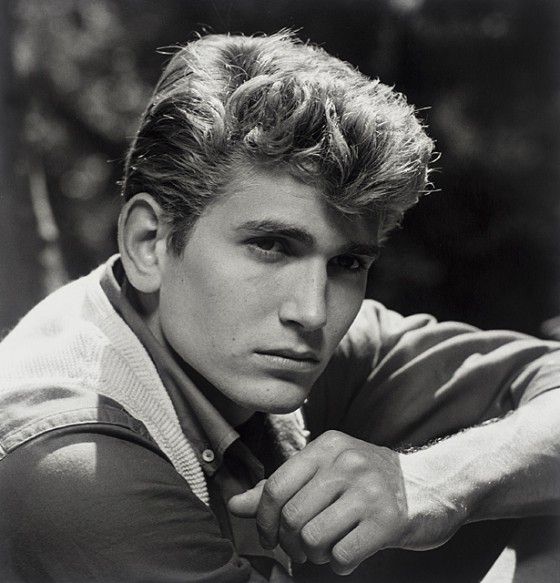 black and white photograph of a young man leaning on a bench with his hand on his chin