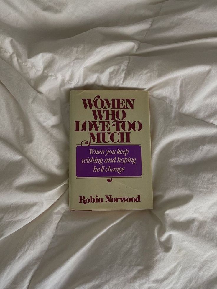 a book on women who love to much is laying on a bed with white sheets