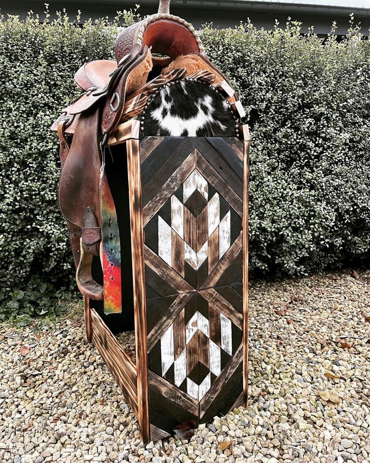 a horse saddle sitting on top of a wooden box in front of some shrubbery