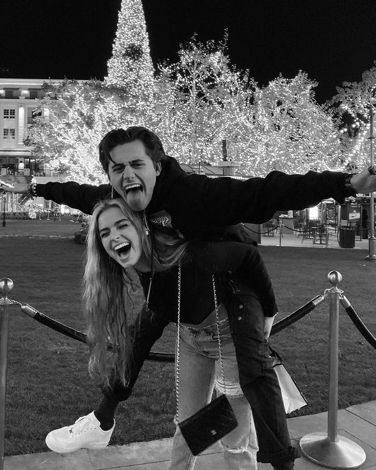 a man and woman posing for a photo in front of a christmas tree at night