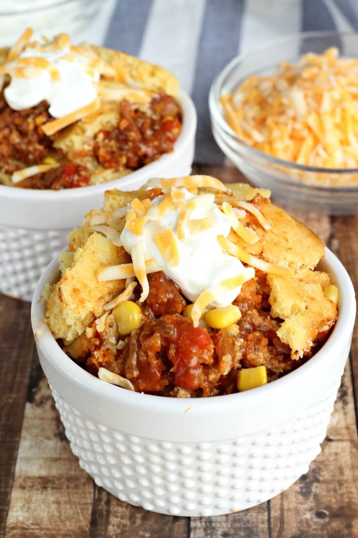 two bowls filled with chili and cornbread casserole on top of a wooden table