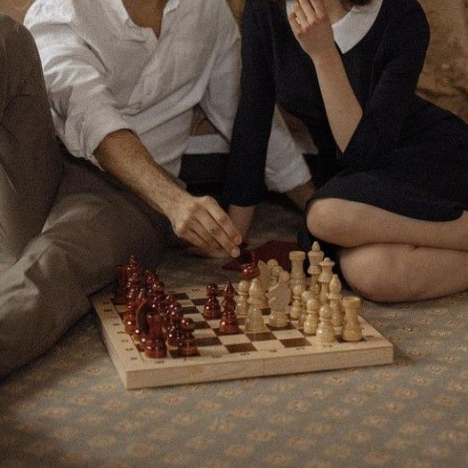 a man and woman sitting on the floor next to a chess board with pieces in front of them