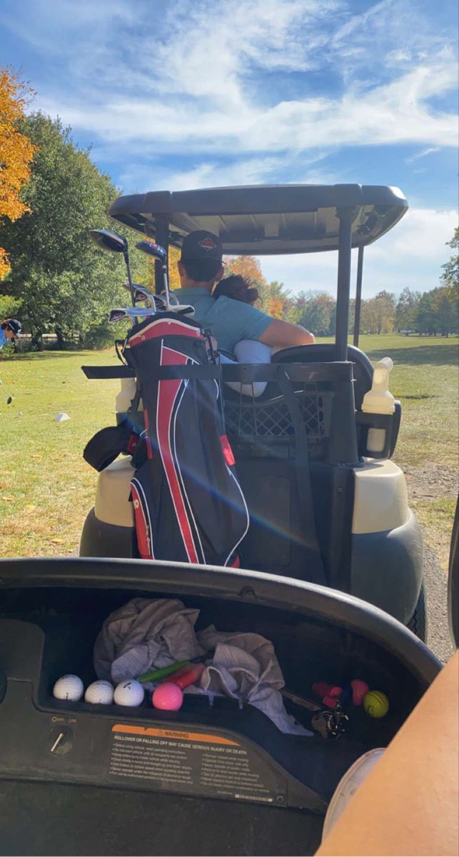 a golf cart filled with bags and balls on the side of a road next to a field