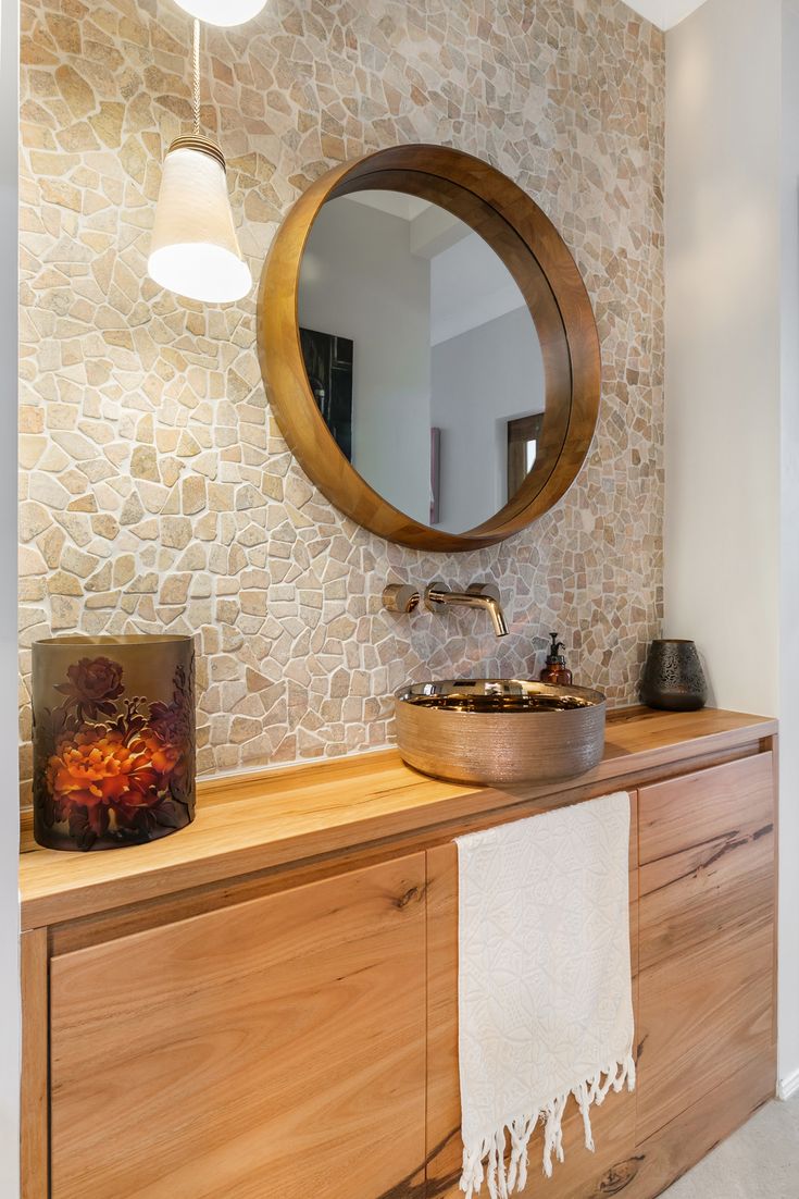 a bathroom with a round mirror above the sink and wooden cabinet below it, along with a white towel hanging from the wall