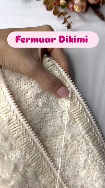 a woman's hand is stitching the side of a white jacket with flowers in the background