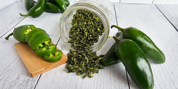 some green peppers are on a wooden board and next to them is a jar of dried herbs