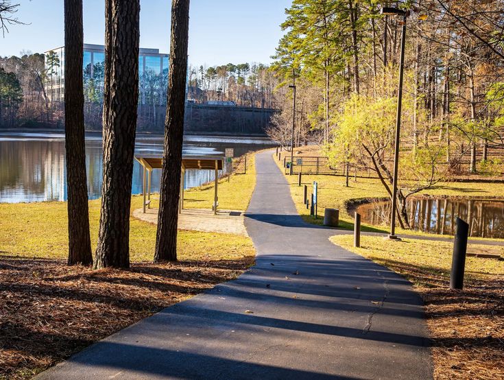 a path in the middle of a park next to a lake with trees on both sides