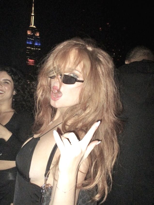 a woman wearing sunglasses making the v sign with her hands at an outdoor party in new york city