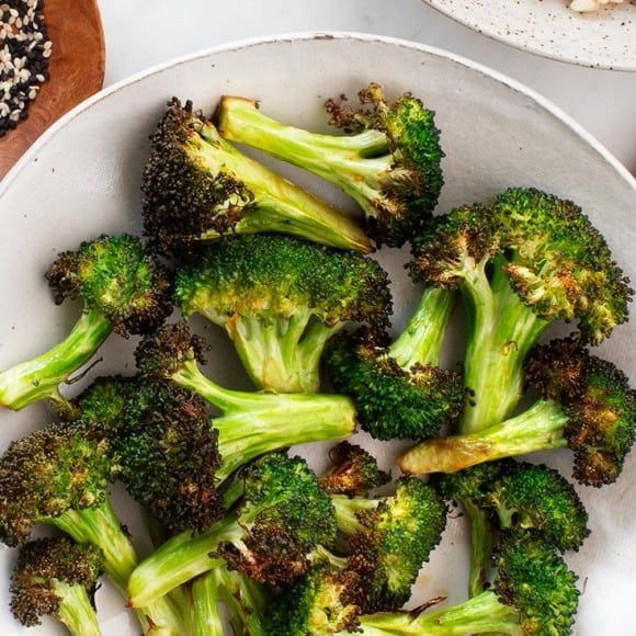 broccoli florets in a white bowl with sesame seeds on the side