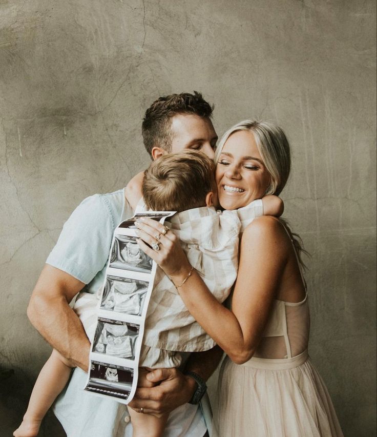 a man and woman holding a baby in front of a wall with pictures on it