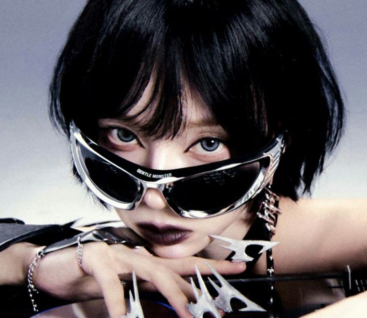 a woman with black hair and sunglasses on her face holding scissors in front of her face