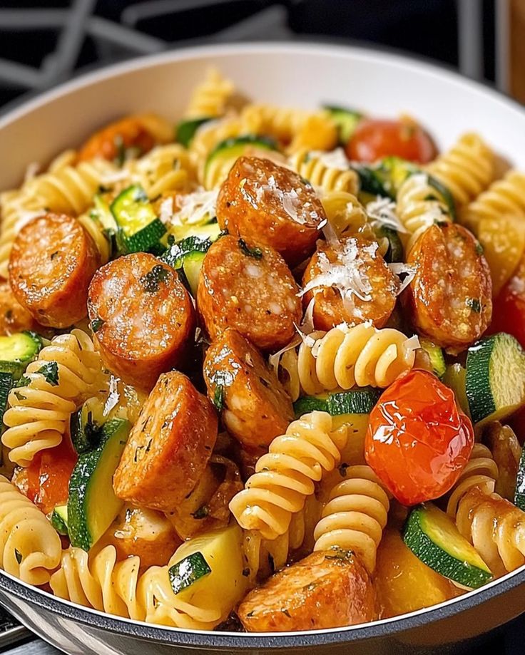 pasta with sausage, zucchini and tomatoes in a white bowl on the stove