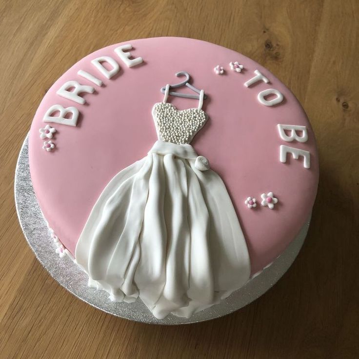 a pink and white wedding cake with the bride's dress on it, sitting on a wooden table