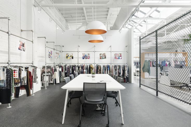 an office with white tables and black chairs in front of the desk is full of clothes