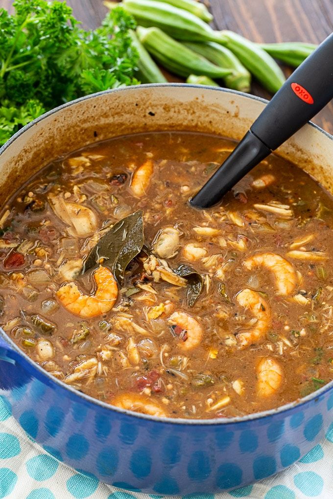 a blue pot filled with shrimp and vegetable soup on top of a table next to green beans