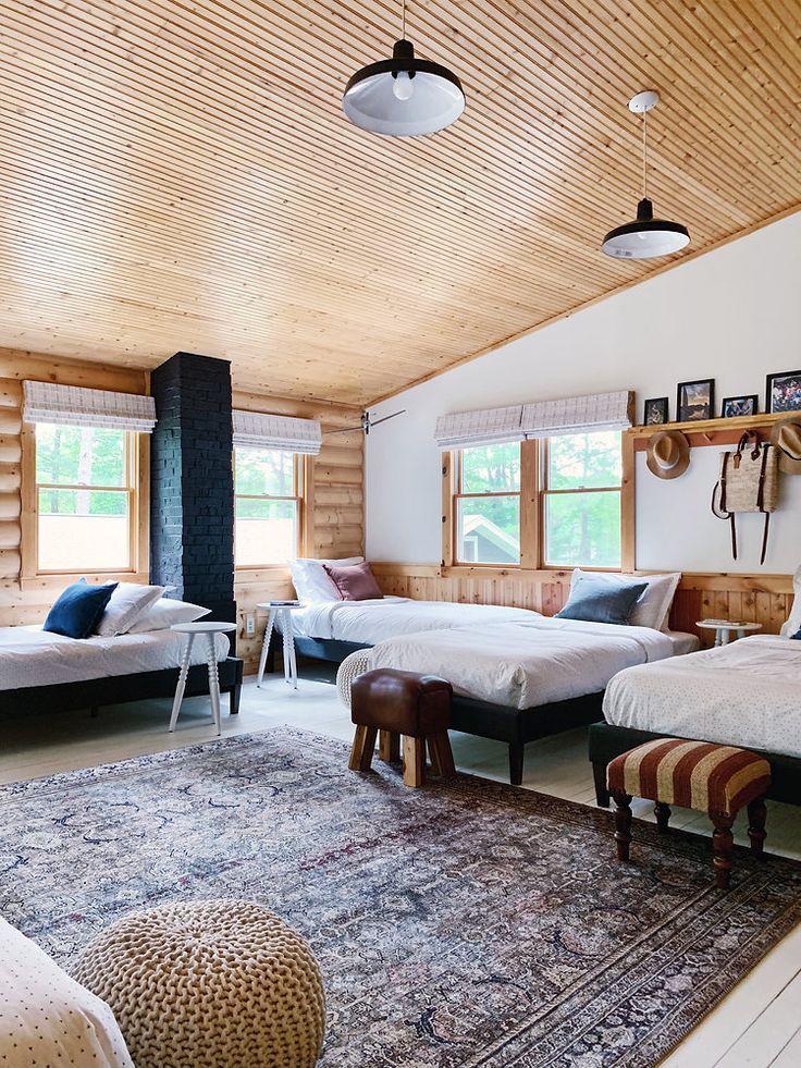 a room with three beds and two stools on the floor in front of windows