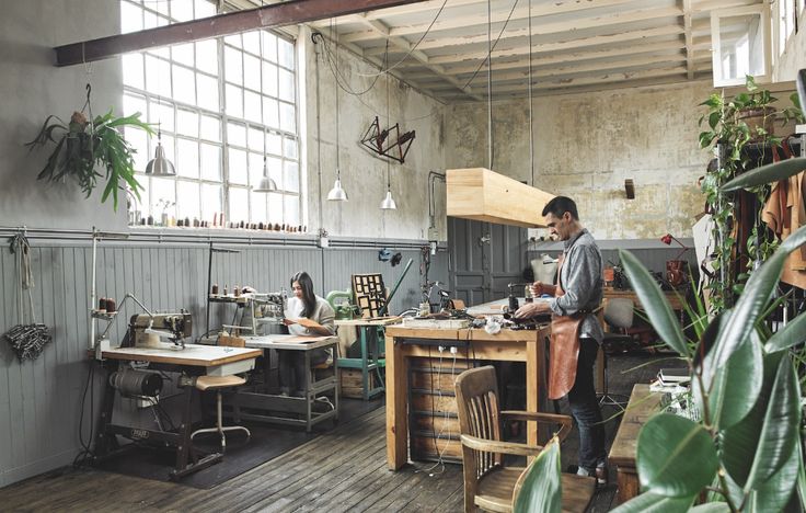 two men are working in an industrial style sewing shop with lots of plants on the tables