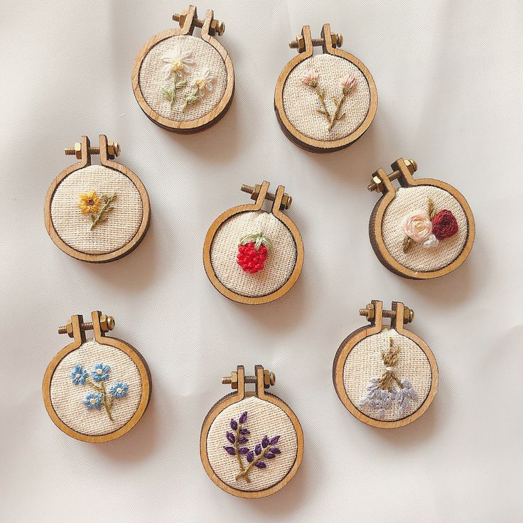 nine embroidered flowers in wooden frames on a white tablecloth, each with different designs and colors