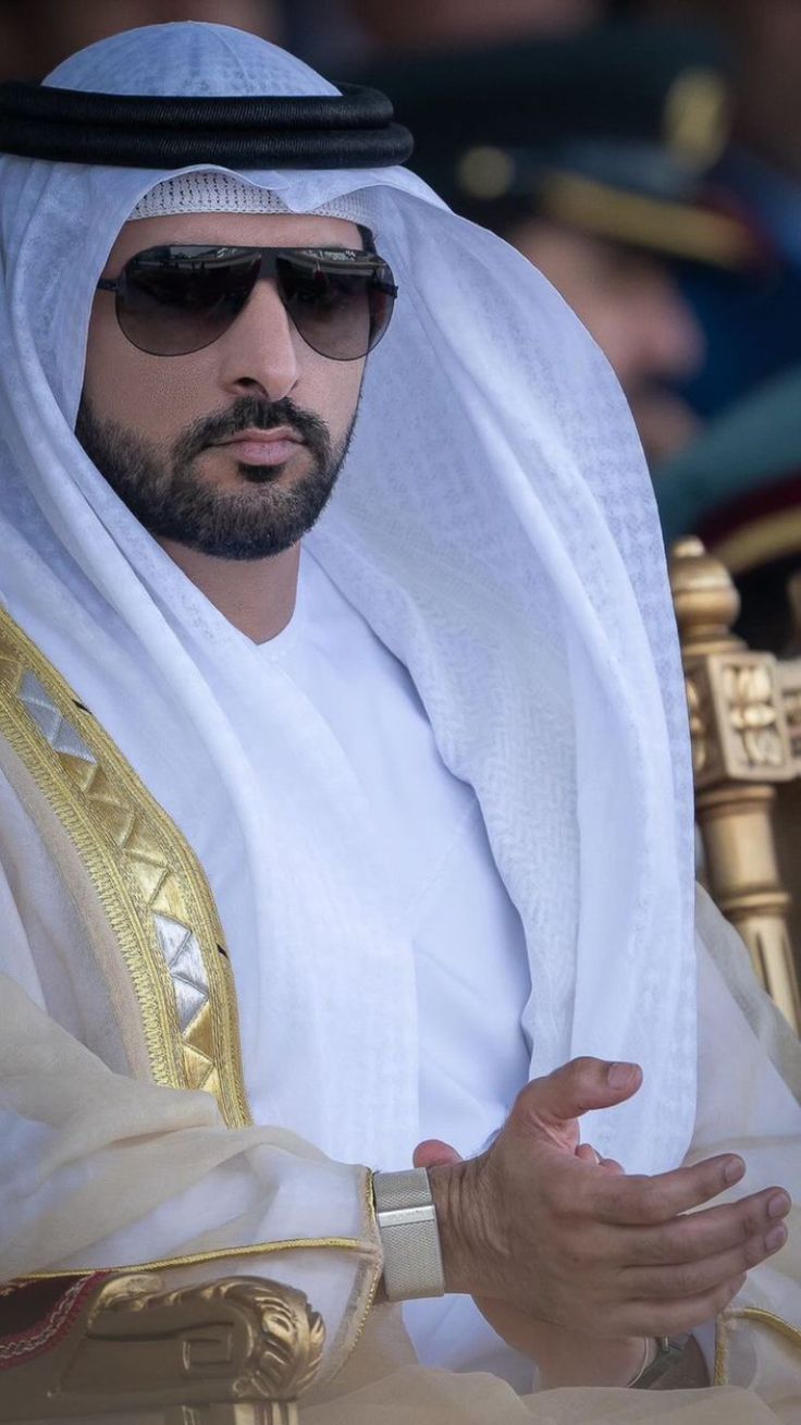 a man wearing sunglasses and a white robe is sitting in a chair with his hands folded out