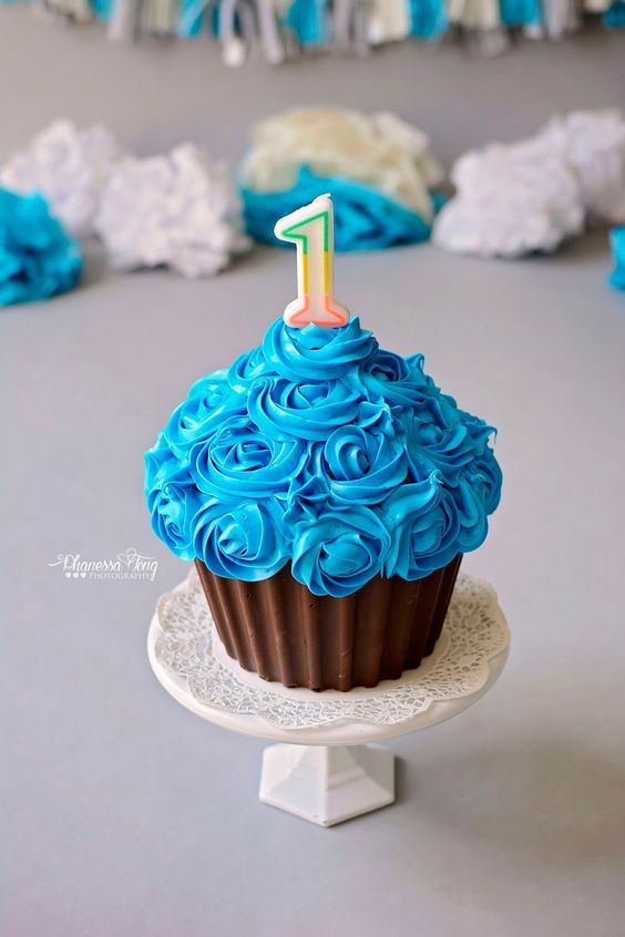 a cupcake with blue frosting and a one on top is sitting on a cake stand