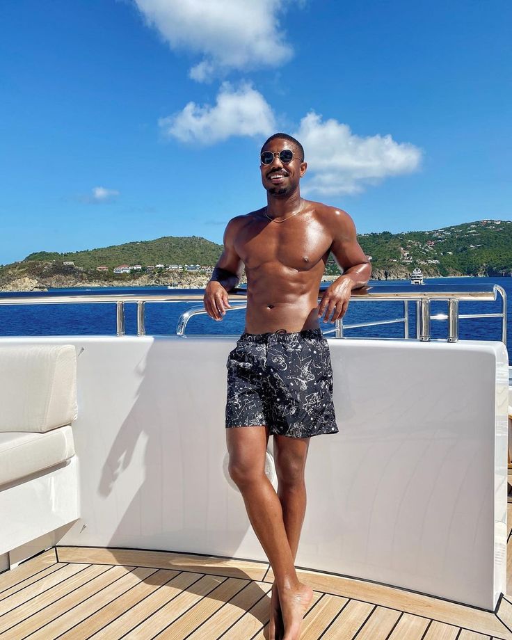 a shirtless man standing on the deck of a boat looking at the camera and smiling