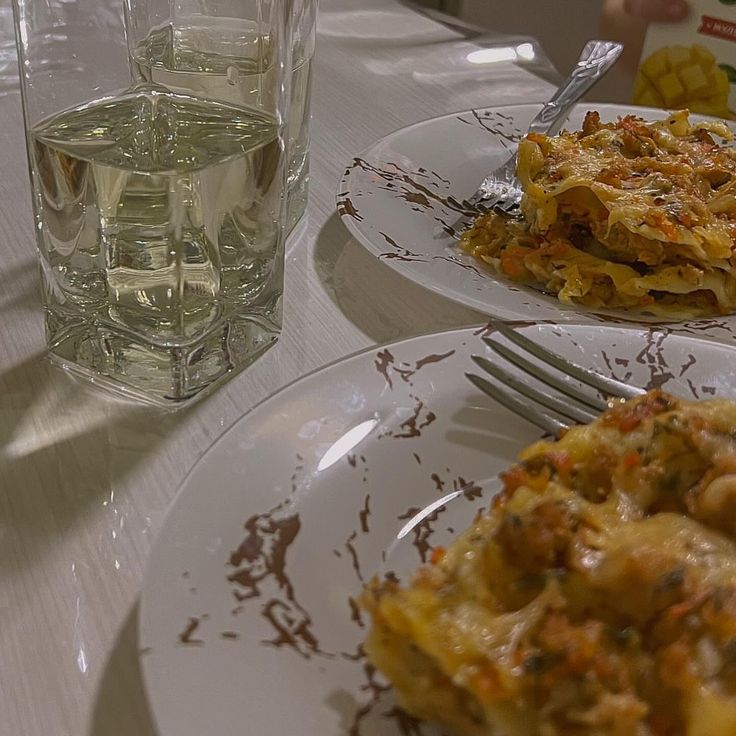 two white plates topped with food next to a glass of water