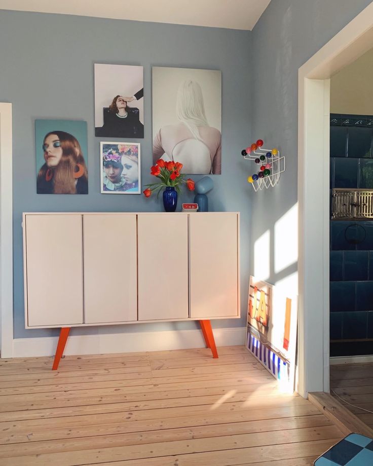 a room with blue walls and pictures on the wall, including an orange sideboard