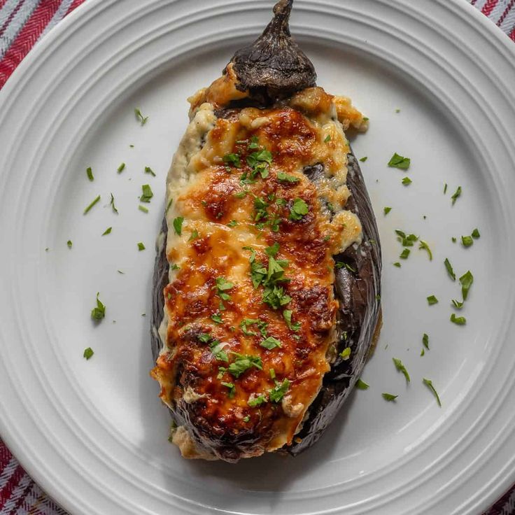 an eggplant stuffed with cheese and parsley on a white plate, ready to be eaten