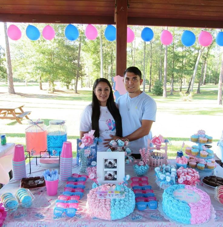 a man and woman standing next to a table full of cakes, cupcakes and decorations