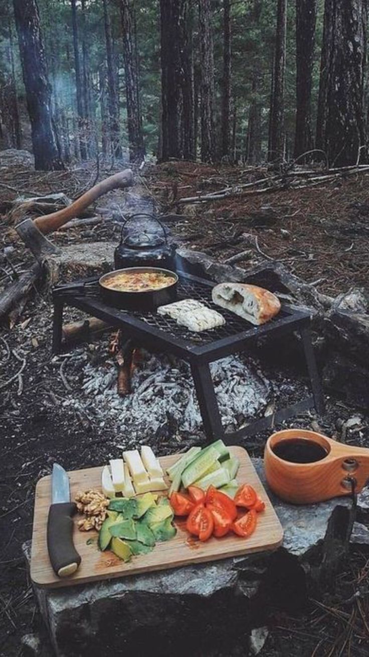 a picnic table with food on it in the woods next to a campfire and fire