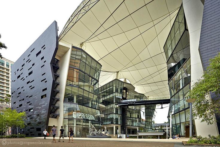 people are walking around in front of a building with glass and metal architecture on it