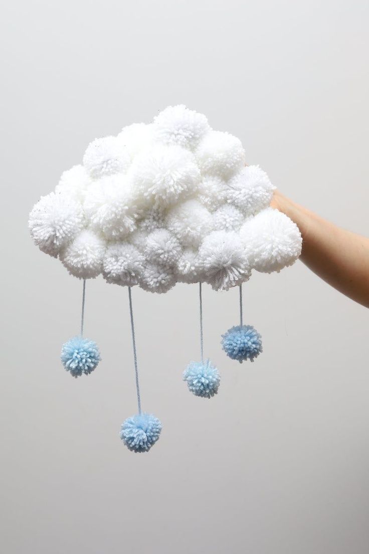 a hand is holding a white cloud with blue pom - poms hanging from it