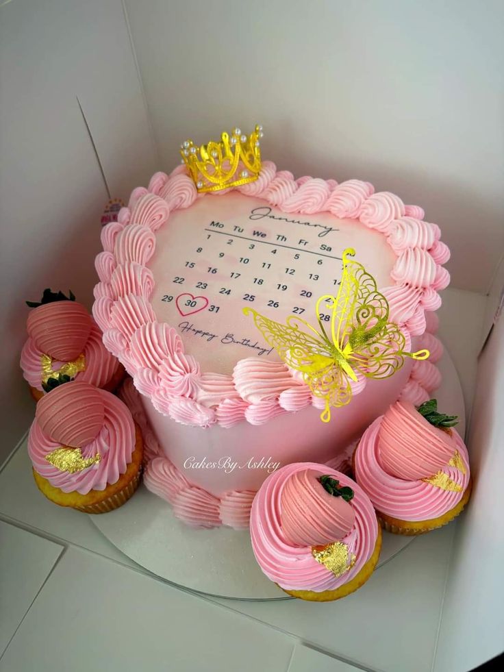 a birthday cake with pink frosting and yellow butterflies on top, surrounded by cupcakes