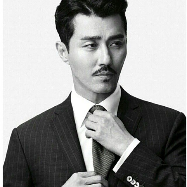 a man in a suit adjusts his tie while posing for a black and white photo