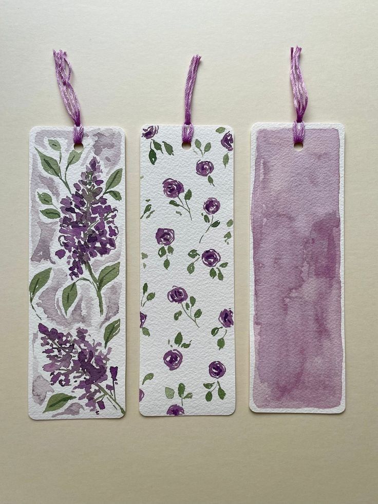 three tags with flowers painted on them are hanging from purple string and one is empty