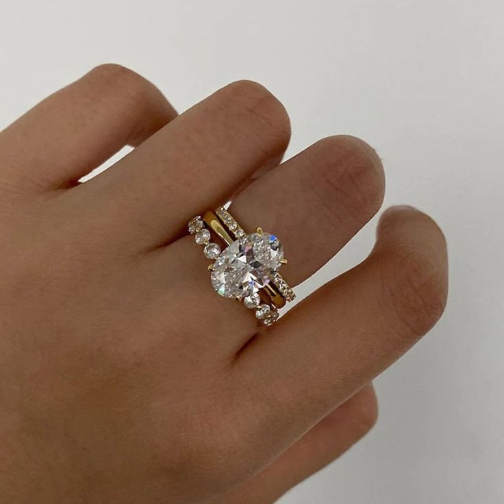 a woman's hand with a diamond ring on top of her finger and the other hand holding an engagement ring