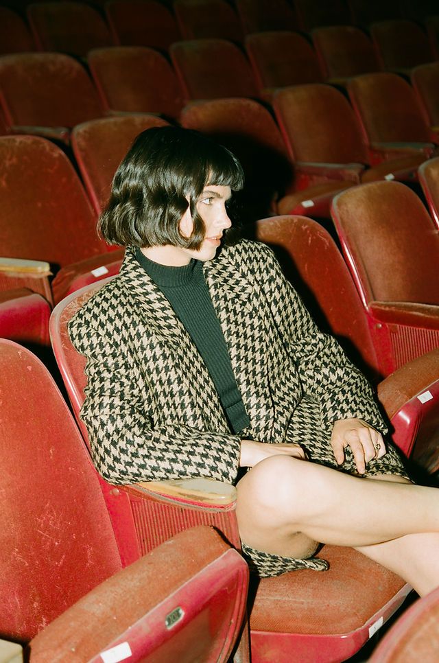 a woman is sitting in an empty theater seat with her legs crossed and looking off to the side