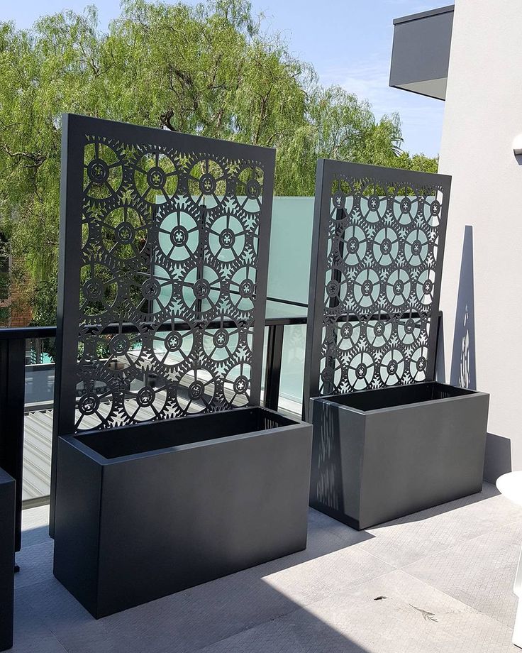 two black planters sitting next to each other on top of a patio with trees in the background